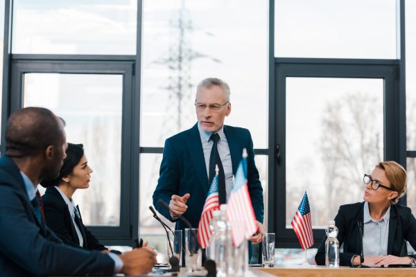 selective focus of bearded businessman pointing with finger at african american diplomat near selective focus of bearded businessman pointing with finger at african american diplomat near